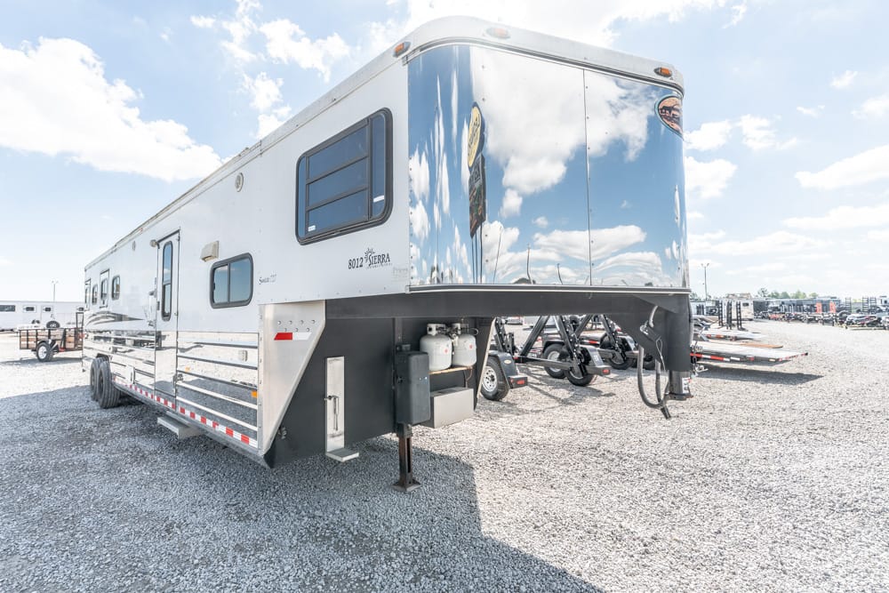 White fifth-wheel RV trailer on a gravel lot, with blue sky and clouds overhead and visible hitch at the front.