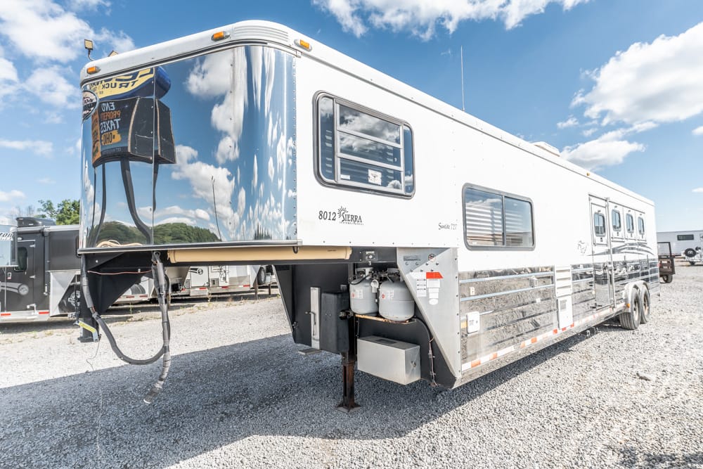 White fifth-wheel RV trailer on a gravel lot with a raised hitch and reflective chrome nose, under a blue sky with clouds.