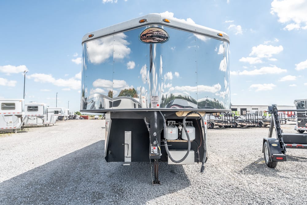 Shiny aluminum semi-trailer in a gravel lot with other trailers and a blue sky behind it