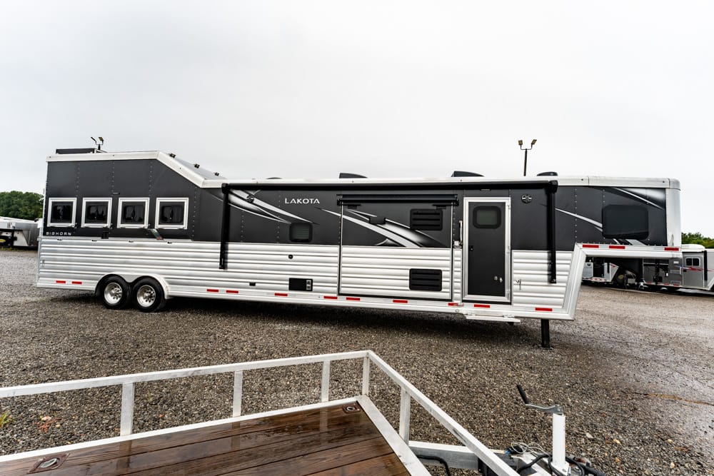 Lakota horse trailer with living quarters, black upper panels and silver corrugated lower wall parked on a gravel lot.