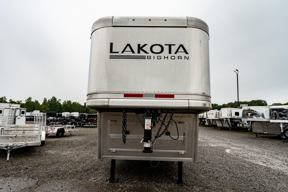 Front view of a Lakota Bighorn horse trailer in a gravel lot, showing the hitch, chains, and steel tongue.