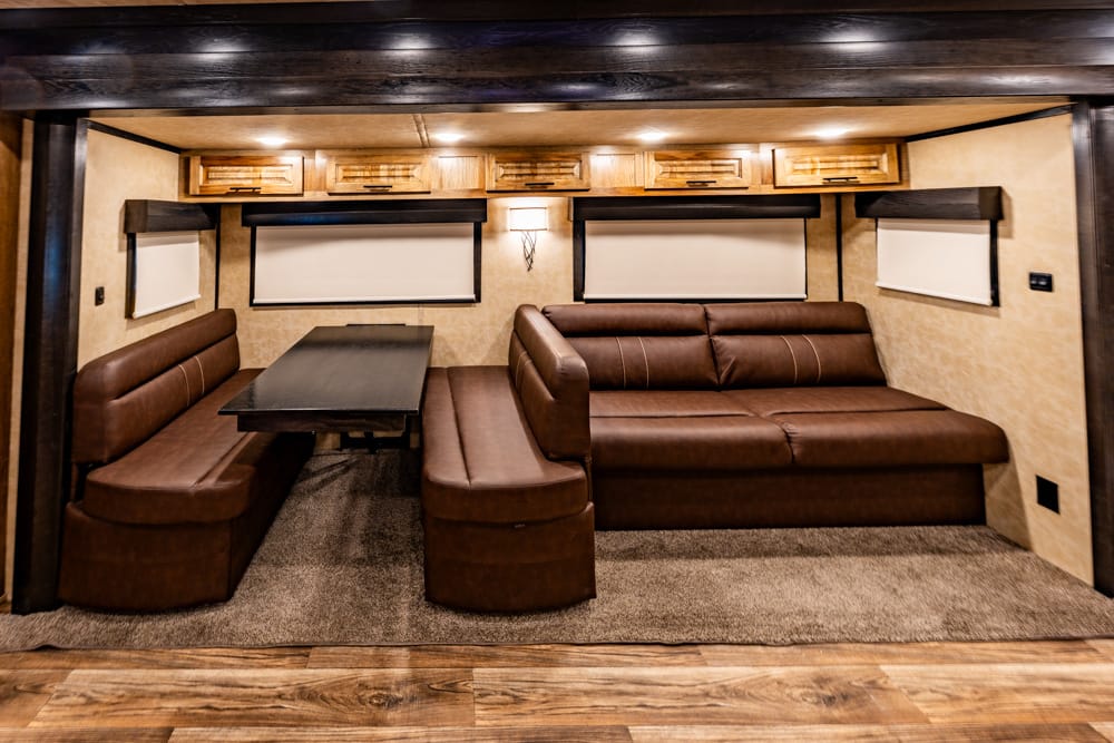 Brown leather U-shaped dining area in an RV with a dark table, beige walls, and overhead cabinets nearby.