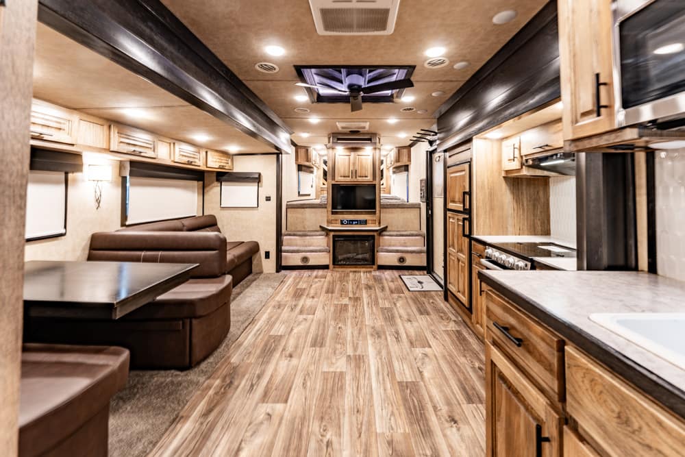 Interior of a luxury RV: living area with brown leather seating, a dining booth, and a central entertainment wall at the far end.