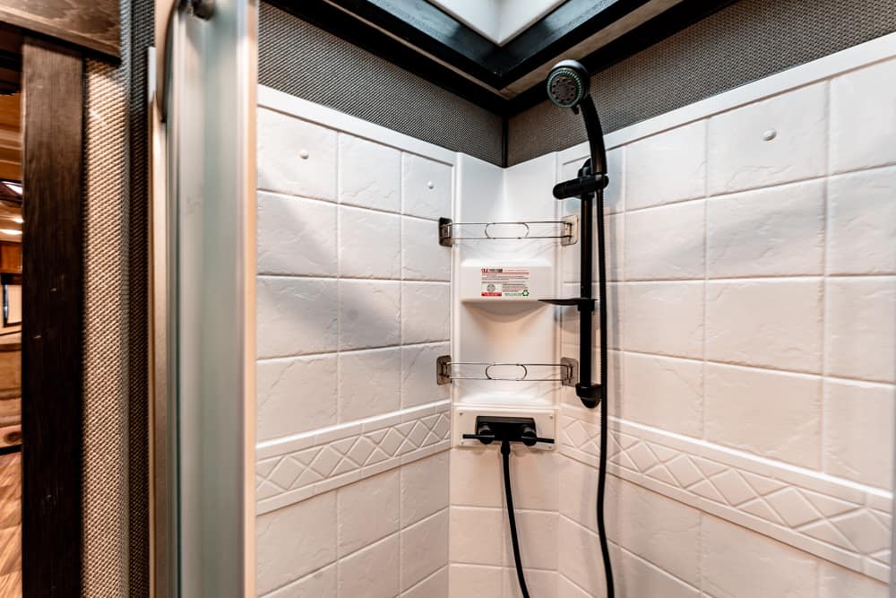 Shower stall with white tiled walls, a handheld showerhead on a vertical rail, and a built-in soap shelf.