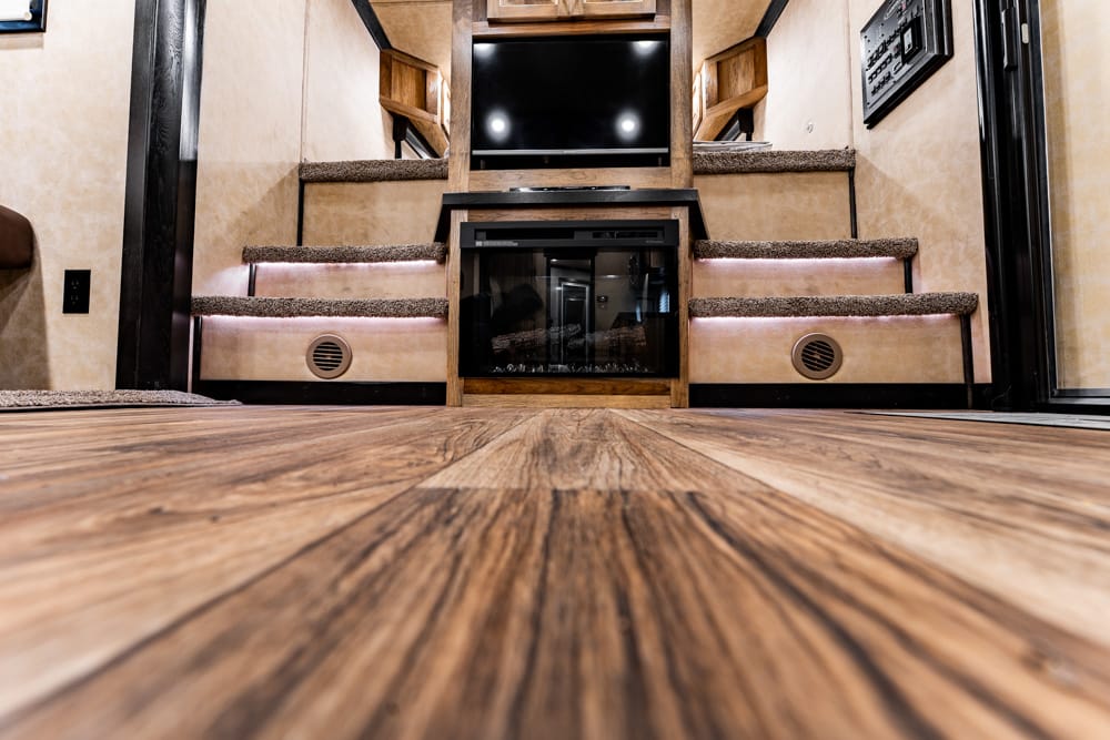 Low-angle view of a wood-trimmed RV interior with a fireplace and TV, and carpeted steps on both sides