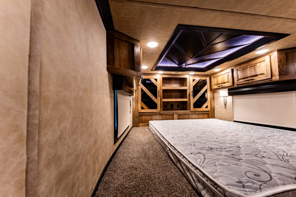 Cozy bedroom inside a wood-toned camper or RV with a queen bed, built-in cabinets, and warm lighting.