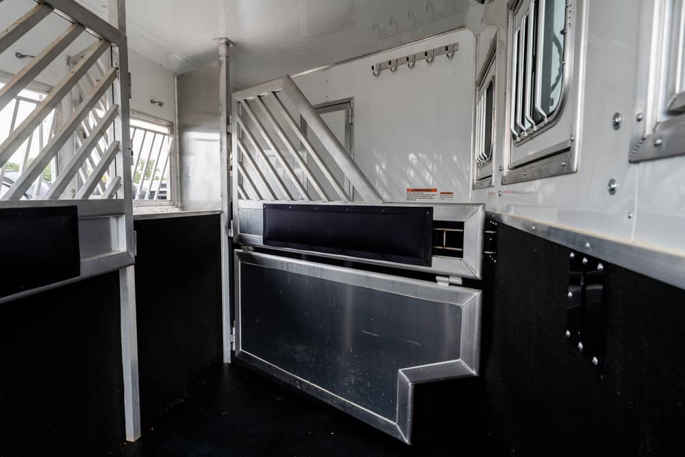 Interior of a metallic livestock trailer with partition rails and a dark padded stall, empty and ready for loading horses or cattle.