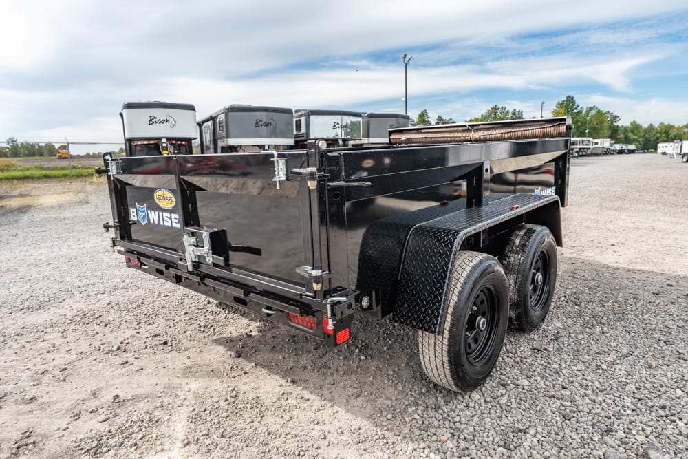 Back view of a black dual-axle utility trailer on a gravel lot, with diamond-plate fenders and a generator rack on top.