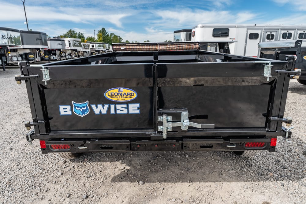 Back view of a black Bow-Wise utility trailer with a Leonard Truck & Trailer logo, showing a sturdy tailgate latch and red rear lights on a gravel lot.