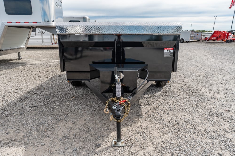 Front view of a black utility trailer with diamond-plate top, hitch and safety chains on a gravel lot.