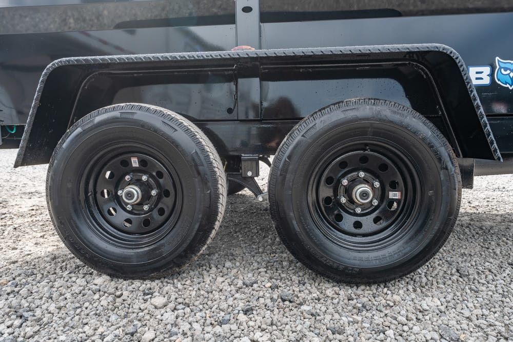 Dual-axle trailer with black steel wheels and a wide fender on a gravel surface.