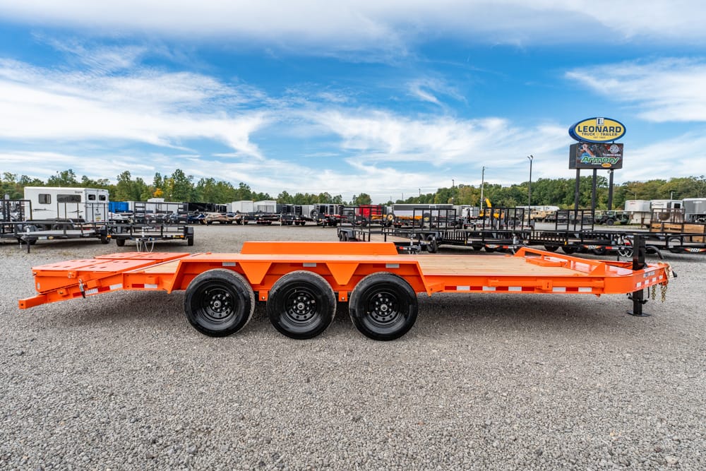 Orange 3-axle flatbed trailer on a gravel lot at a trailer dealership, with other trailers in the background and a blue sky above