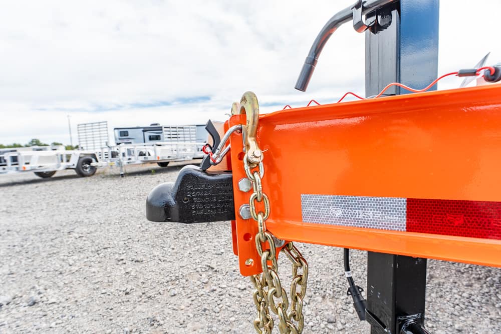 Safety chain and padlock securing an orange trailer hitch at a truck and trailer lot.