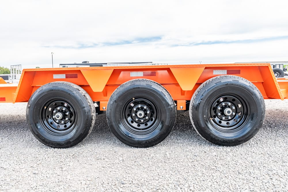 Orange multi-axle heavy-duty trailer with three black wheels on a gravel surface