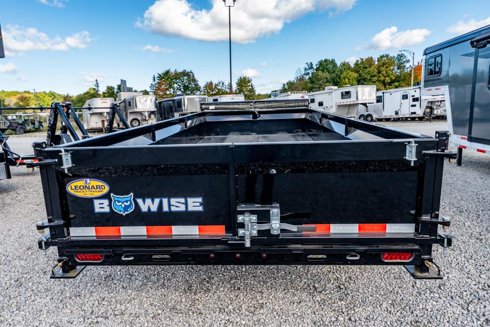 Black BowWise dump trailer in a gravel lot with red/white reflective stripes and a rear latch.