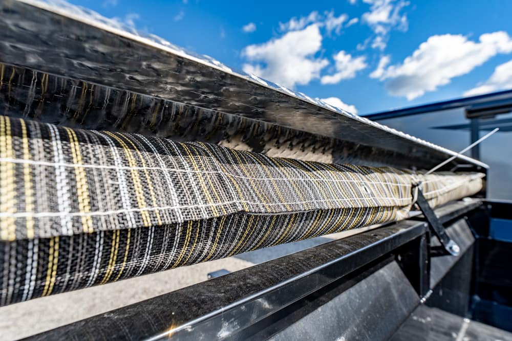 Close-up of a striped woven conveyor belt on a metal frame outdoors against a blue sky.