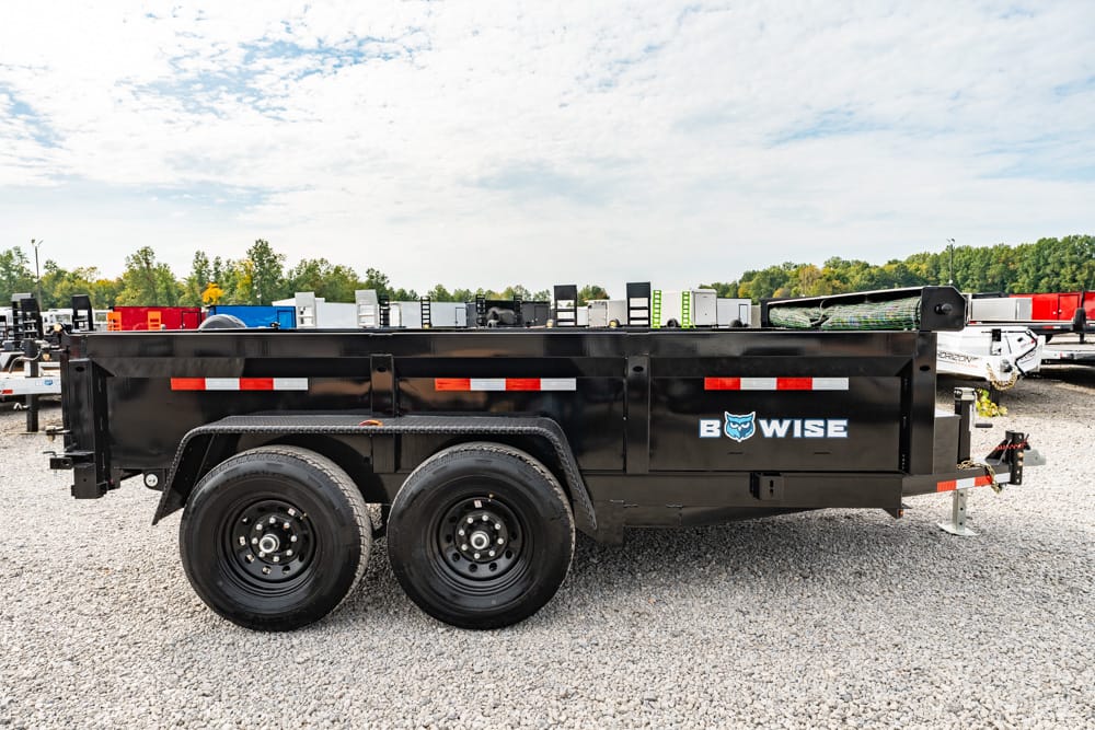 Black dual-axle dump trailer on a gravel lot with red/white reflectors and a BOWISE logo visible against a row of trailers in the background.