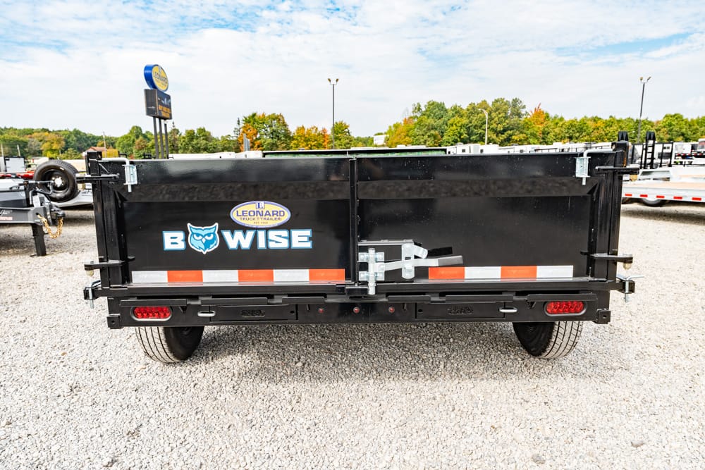 Rear view of a black Bowise utility trailer with orange and white reflective strips, parked on a gravel lot.