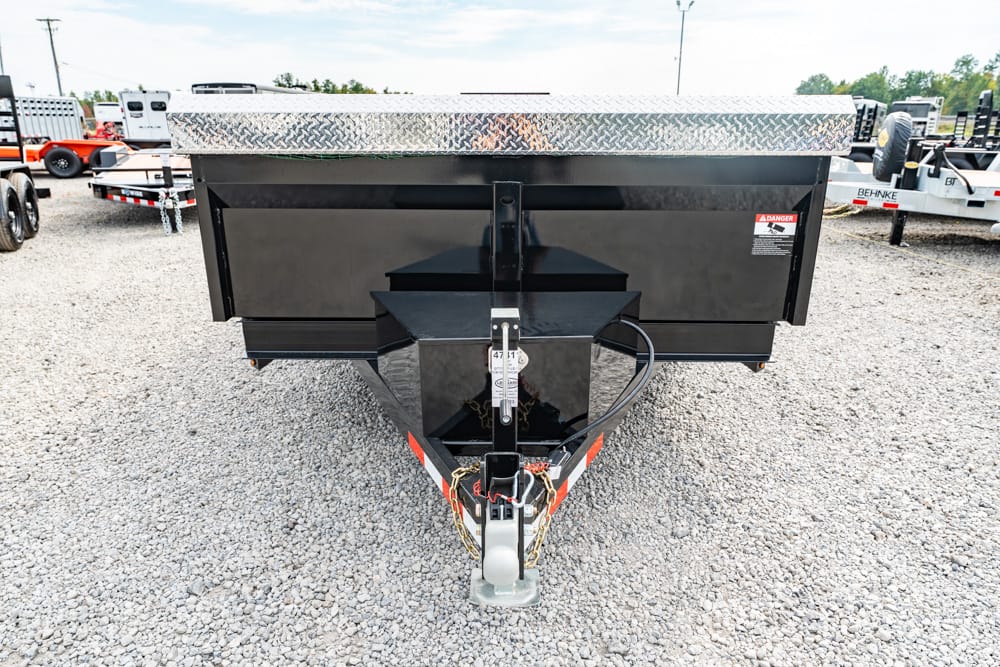 Front view of a black dumping trailer with a silver diamond-plate top, hitch and safety chains in a gravel lot.