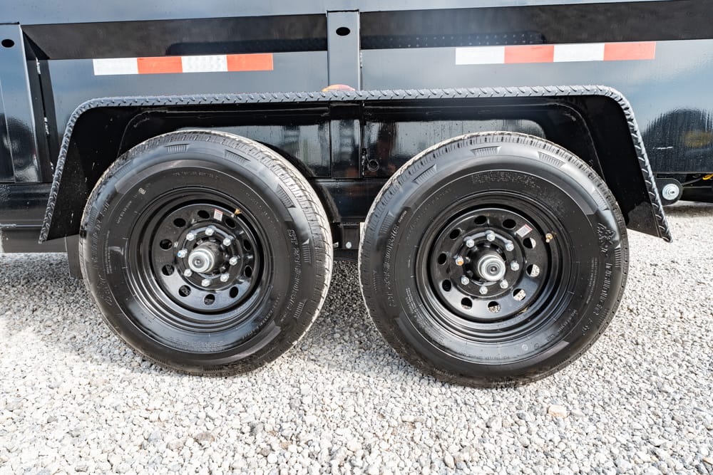 Dual-axle trailer wheels with black steel rims on a gravel surface under a black trailer fender
