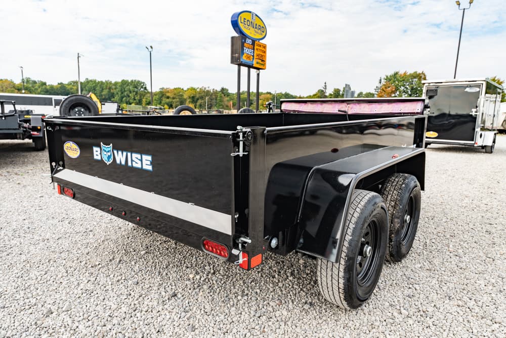 Black dual-axle dump trailer with 'BOWISE' logo and owl graphic, parked on gravel at a trailer lot.