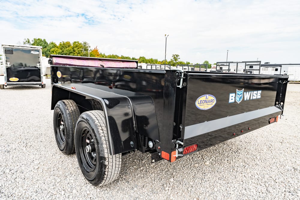 Black dual-axle utility trailer with wheel wells, parked on gravel; logos for Leonard and Bowise visible on side.