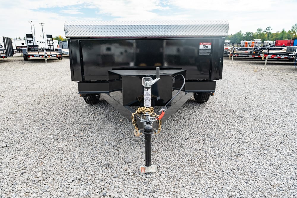 Front view of a black utility trailer on a gravel lot, showing the hitch, safety chains, and trailer jack at the tongue.