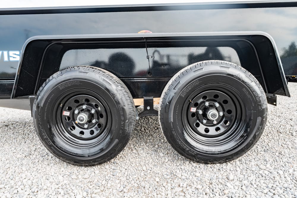 Dual-axle trailer with black steel wheels and tires on a gravel surface
