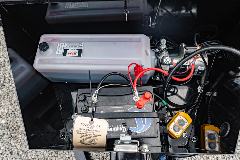 Open battery compartment with a car battery connected by red and black cables, a white reservoir, and yellow meters in a black chassis.