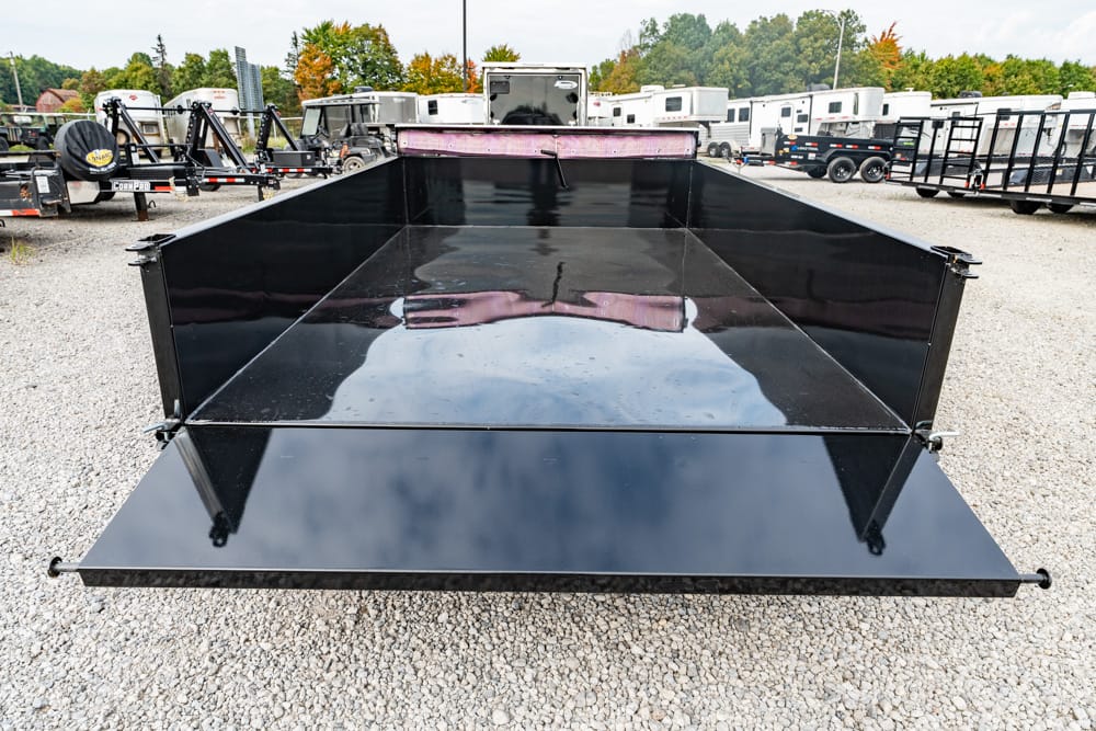 Wide view of a black dump trailer bed parked on a gravel lot, with other trailers and RVs visible in the background.