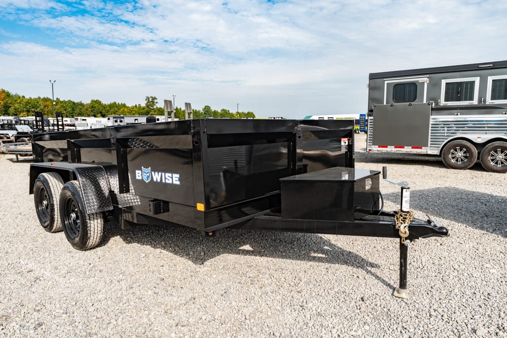 Black dual-axle dump trailer on a gravel lot with a front hitch and jack stand, ready for towing