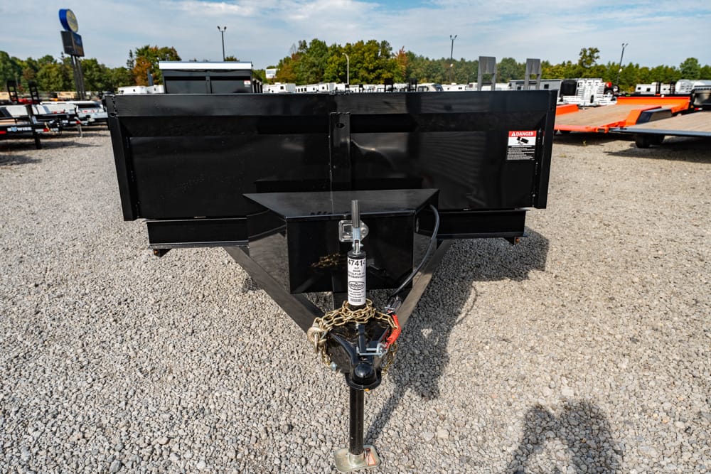 Front view of a black utility trailer with its hitch and safety chains on a gravel lot, other trailers in the background.