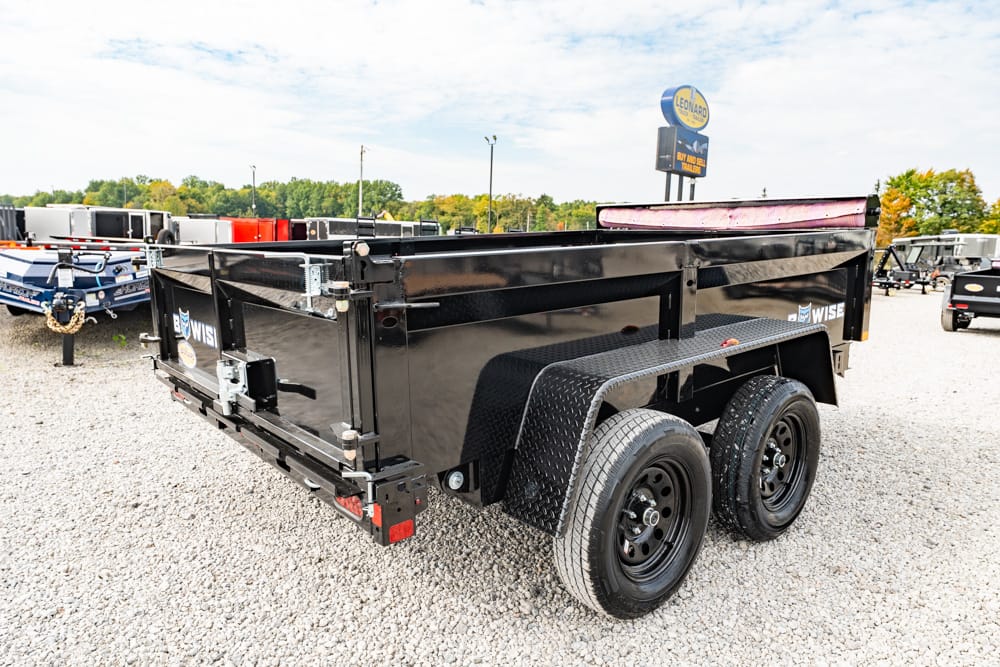 Black dual-axle dump trailer on a gravel lot, with diamond-plate fenders and rear gate closed.