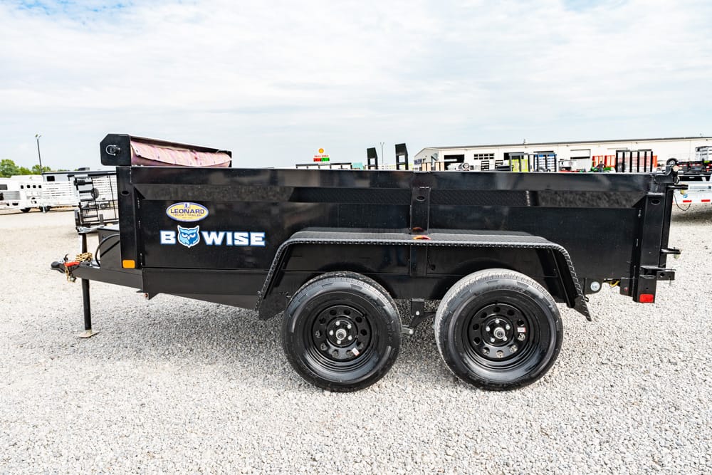 Black dual-axle dump trailer on a gravel lot with BowWise branding visible on the side.