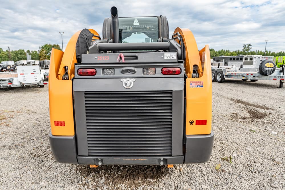 Front view of an orange and gray telehandler on a gravel lot, with trailers visible in the background.