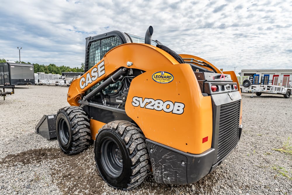 Orange CASE SV280B skid steer loader parked on a gravel lot with other equipment in the background.