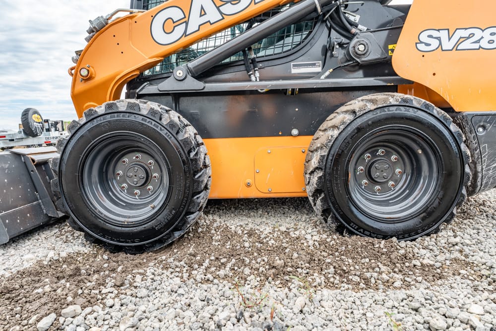 Close-up of large rugged tires on an orange construction machine on a gravel surface, showing wear from work site use.