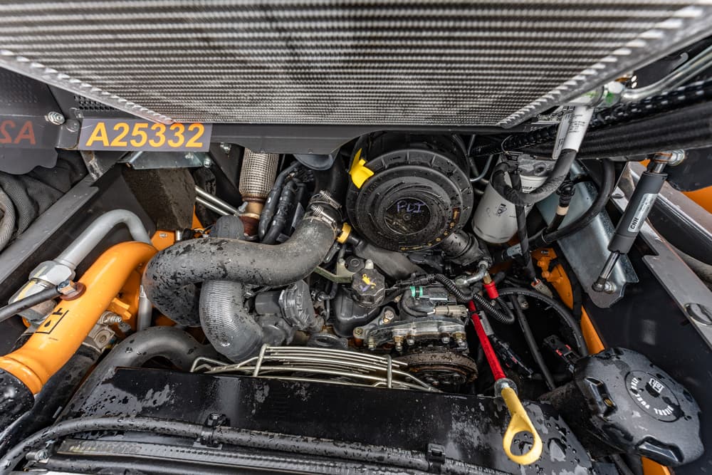 Close-up of an engine bay in an orange-frame machine, showing hoses, belts, and a round air filter housing labeled A25332 nearby.