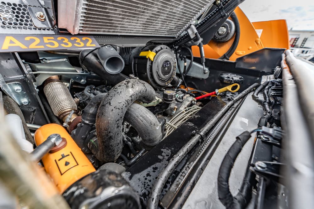 Close-up of a large vehicle engine bay with exposed hoses, a radiator, and an orange safety component in the foreground.