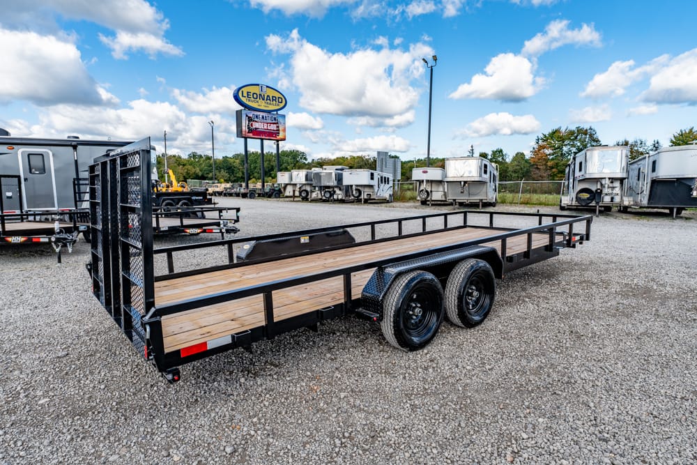 Long black flatbed trailer with a wooden deck and dual axles parked on a gravel lot.