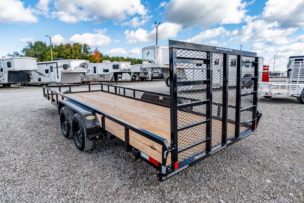 Black utility trailer with a wood deck and dual axles parked on a gravel lot, ready for hauling equipment or vehicles.