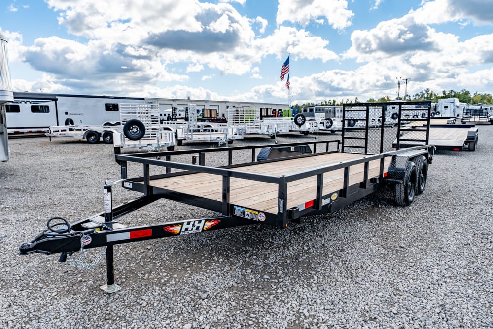 Black utility trailer with a wooden deck and dual axles on a gravel lot, ready for hauling in a trailer yard.