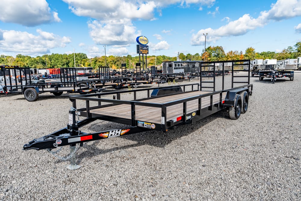 Flatbed utility trailer with wooden deck and side rails in a gravel lot, with other trailers in the background.