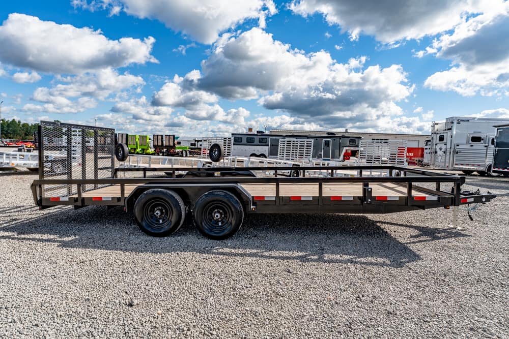 Flatbed trailer with dual rear wheels parked in a gravel lot, with other trailers and trucks in the background.