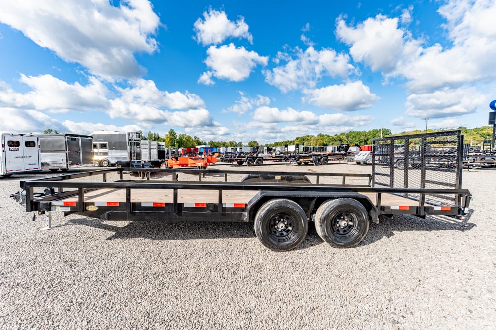 Open flatbed trailer with wooden deck and side rails on a gravel lot, dual-axle wheels visible in the foreground.
