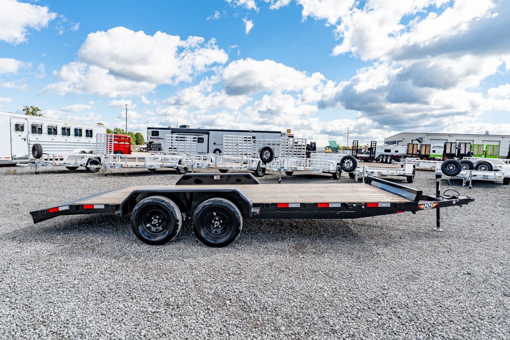 Flatbed double-axle trailer on a gravel lot with other trailers in the background, under a blue sky.