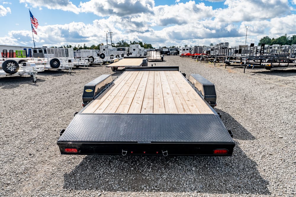 Wide view of a trailer lot with a wood-deck flatbed trailer in the foreground and rows of trailers behind it under a blue sky.