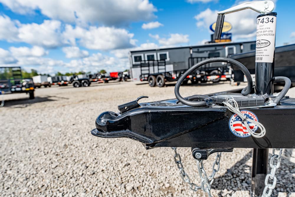 Close-up of a black trailer hitch on a gravel lot with safety chains and a raised jack, American-made sticker visible.