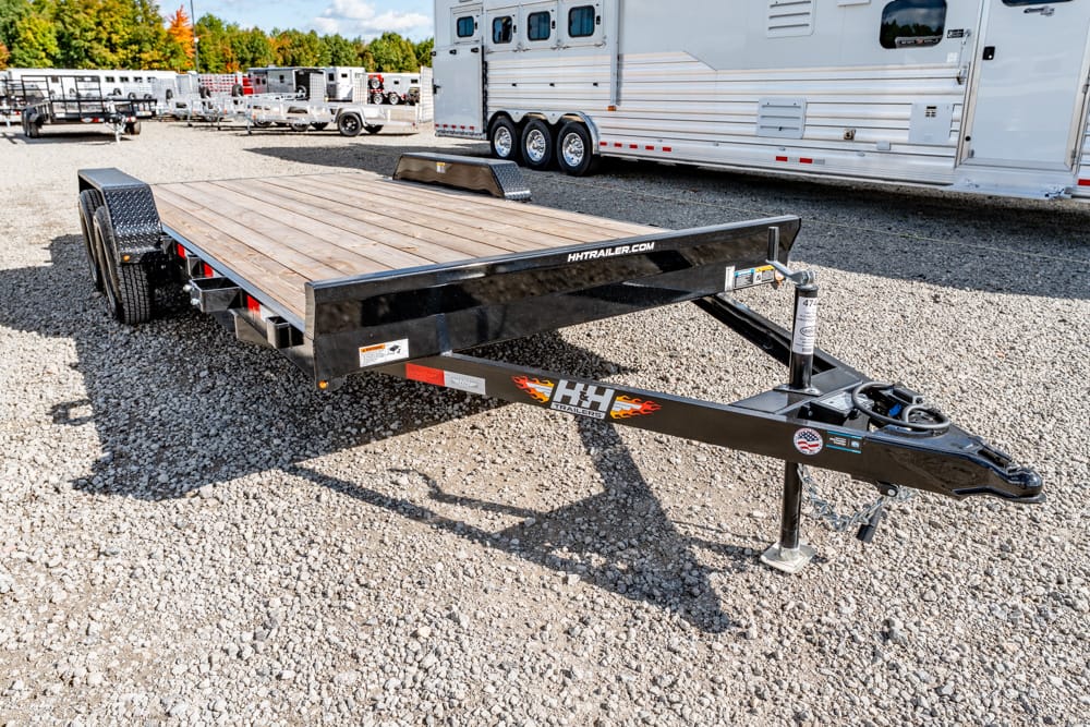 Black flatbed trailer with a wood deck and dual axles parked on a gravel lot among other trailers.