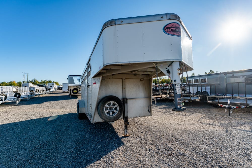 A gooseneck trailer parked on gravel yard with other trailers in the background under a clear blue sky.